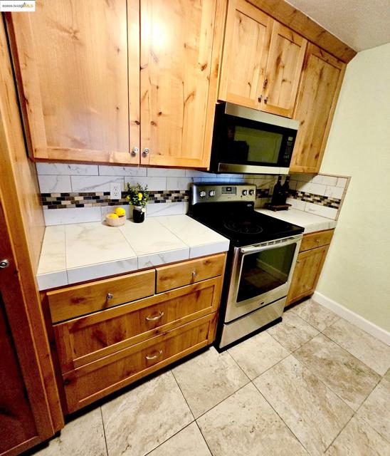 Kitchen with tile counters, appliances with stainless steel finishes, backsplash, and light tile patterned floors