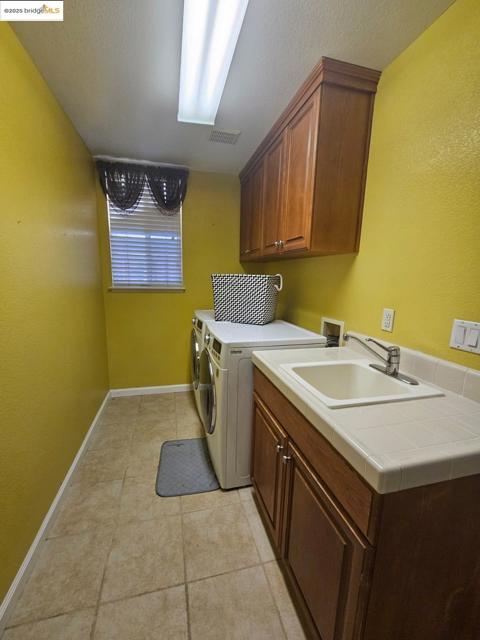 Laundry room with cabinet space, washing machine and clothes dryer, light tile patterned floors, and a textured ceiling