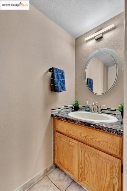 Bathroom featuring a textured wall, tile patterned flooring, vanity, and a textured ceiling