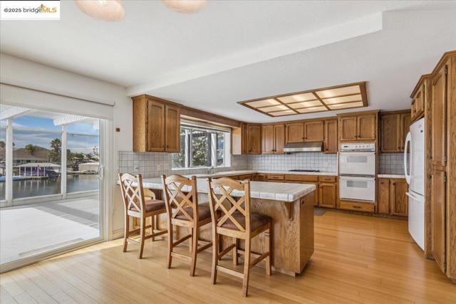 Kitchen featuring brown cabinets, backsplash, a kitchen breakfast bar, and white appliances