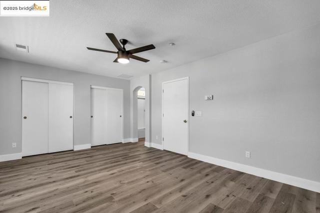 Unfurnished bedroom with multiple closets, arched walkways, wood finished floors, a textured ceiling, and a ceiling fan