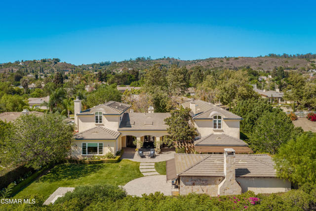 Aerial view of a beige stucco home with tiled roofs, landscaped grounds, and rolling hills beyond.