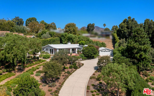 1950s charm meets bright, open sophistication in this very private Point Dume home. Set high on a hill behind gates at the end of a long drive among walking gardens, palms, and fruit trees on approximately one acre, the property includes Riviera 2 beach rights. The main living areas feature high, sloped ceilings with beams and trusses, long picture windows facing onto wraparound patios and landscaping, plus custom-finished cement floors. The spacious living room, with a beamed ceiling and a brick fireplace, has a wall of glass looking out at the tranquil, private front yard. A wide doorway opens into the kitchen/dining great room, with windows on two sides and a glass door providing easy flow to the back patio for al fresco dining. The kitchen is beautifully updated, with stone countertops, superb appliances, bar seating, and a pantry. The home's two en-suite bedrooms include a primary suite with a skylight and a peaceful lounge. The outdoor areas are equally inviting and include a shaded portico at the front of the house overlooking the long expanse of gardens, a side yard with a fire pit and outdoor seating, plus a lighted back patio with flagstone pavers, and a large dining and barbecue area. This leads to a landscaped terrace with a hot tub and vegetable beds with custom covers. At the front of the house, the two-car garage has been converted into a bonus guest studio/office. As a serene getaway or welcoming home for entertaining, this is an exceptional property filled with charm and light.
