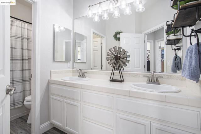 Full bath with double vanity and laminate wood-type flooring, with door separation of vanity and shower.