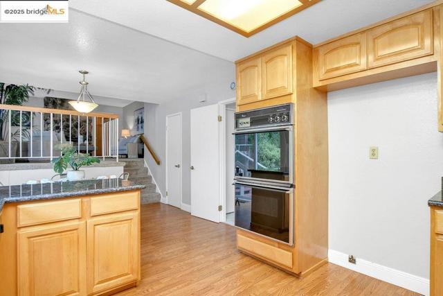 Kitchen with light brown cabinets, dark stone counters, pendant lighting, and light wood finished floors