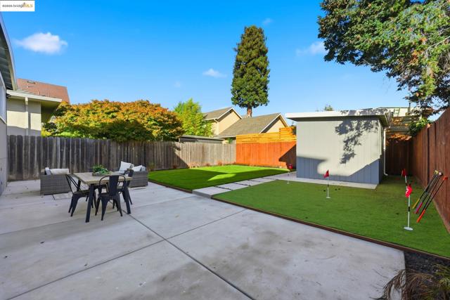 Fenced backyard featuring a patio, a putting area, and a storage shed