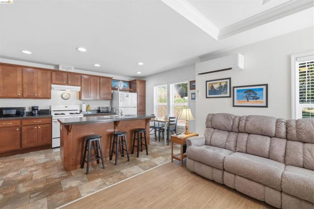 Open-concept living space with a kitchen island featuring seating, wood-finish cabinetry, recessed lighting, and a tray ceiling