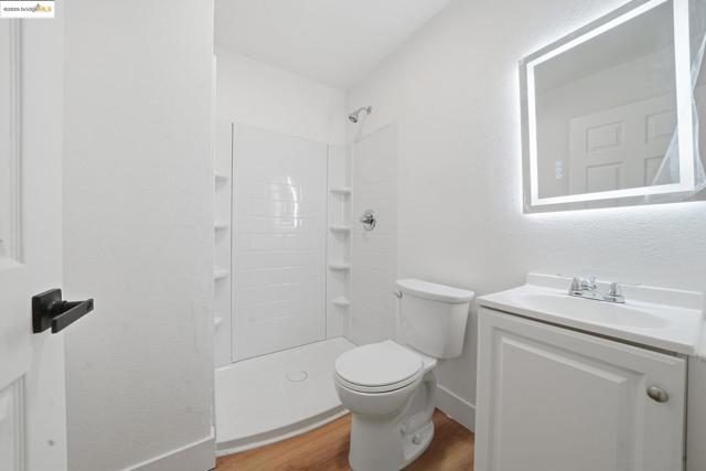 Bathroom with light wood-style flooring, a shower stall, a textured wall, and vanity