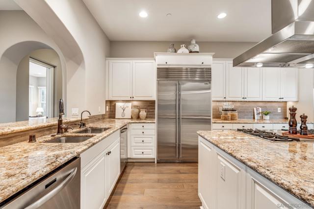 Gourmet kitchen with a spacious island, granite countertops, high-end appliances, and custom cabinetry. Open-concept design flows into the living area, perfect for entertaining. Warm wood flooring and a statement range hood add elegance and functionality.