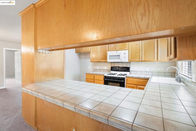 Kitchen featuring gas stove, white microwave, carpet floors, and tile counters