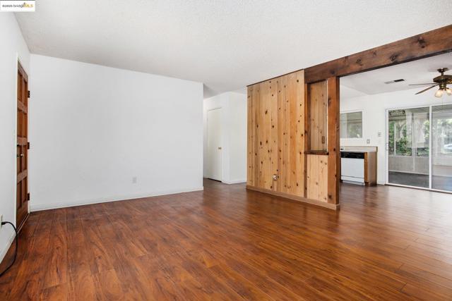 Unfurnished living room featuring dark wood-style floors, a ceiling fan, a textured ceiling, and beam ceiling
