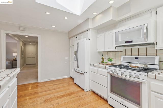 Kitchen with tile countertops, white appliances, a skylight, tasteful backsplash, and white cabinets