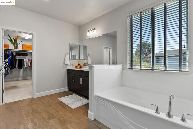 Bathroom featuring vanity, a garden tub, a spacious closet, and wood finished floors