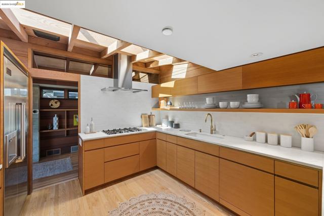 Kitchen with open shelves, modern cabinets, decorative backsplash, light wood-style flooring, and ventilation hood