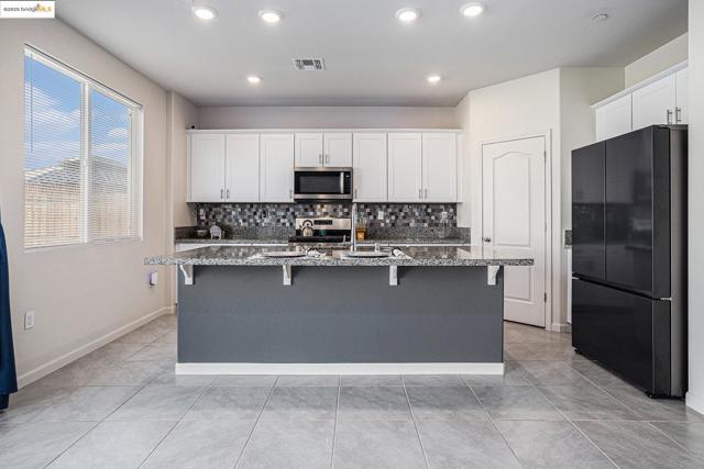 Kitchen featuring stainless steel appliances, dark stone counters, white cabinetry, backsplash, and a kitchen breakfast bar