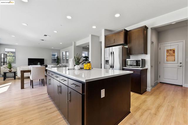 Kitchen featuring dark brown cabinetry, light countertops, a center island, stainless steel microwave, and light wood-type flooring