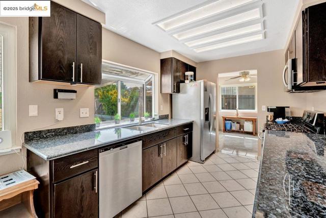 Kitchen featuring appliances with stainless steel finishes, dark brown cabinets, light tile patterned floors, ceiling fan, and dark stone counters