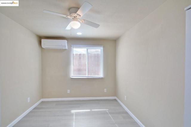 Bedroom with a wall mounted AC, ceiling fan, and light wood-style floors