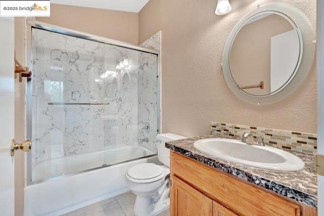 Bathroom featuring a textured wall, shower / bath combination with glass door, vanity, tile patterned floors, and tasteful backsplash