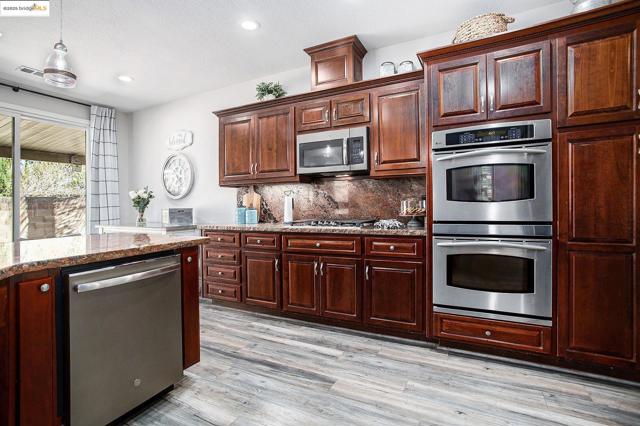 Kitchen featuring appliances with stainless steel finishes, double oven, 5 gas burner stovetop, tasteful backsplash, stone countertops, laminate wood-style floors, and pendant lighting