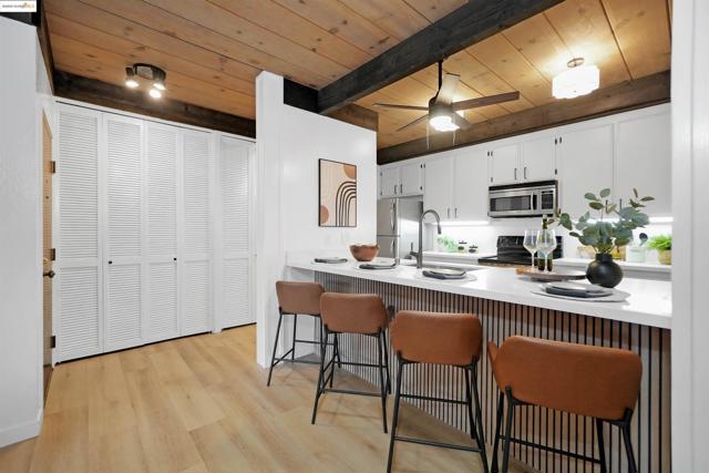 Kitchen featuring a wooden ceiling with exposed beams, a breakfast bar, white cabinets, light wood-style floors, and appliances with stainless steel finishes
