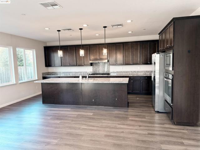 Kitchen with dark brown cabinets, decorative light fixtures, an island with sink, dark wood-style flooring, and recessed lighting
