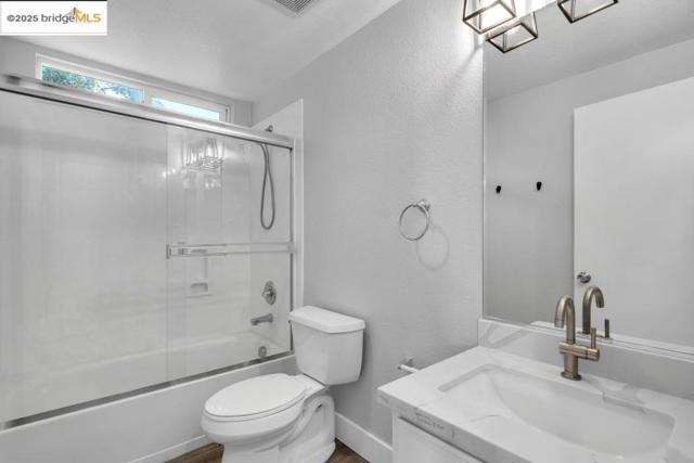 Full bathroom featuring a textured wall, vanity, and shower / bath combination with glass door
