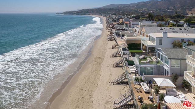 Discover the epitome of coastal living in this Malibu Colony beachfront hideaway. This home boasts beautiful natural light and hardwood floors throughout. With two primary suites featuring panoramic ocean views and two additional bedrooms with mountain views, this home encompasses 4,959 square feet of living space across an open-concept floorplan. The chef's kitchen offers a Wolf range, two sinks, and a large center island ready for cooking or entertaining. The adjacent living room features architectural details, including built-in arched bookshelves. A wall of French doors opens to a sunny deck for effortless indoor/outdoor living. A two-car garage and a deep driveway provide for ample parking. Additional features include a built-in BBQ, wood deck, Jacuzzi, and direct beach access, while Malibu's best shops and restaurants, including Nobu and SoHo House, are just a stone's throw away. Nestled in a 24-hour guard-gated community, security and privacy are paramount. Seize this rare opportunity to embrace the ultimate beachfront lifestyle in one of Malibu's exclusive enclaves.