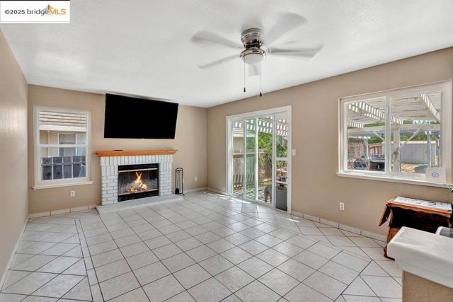 Unfurnished living room featuring light tile patterned flooring, a ceiling fan, a brick fireplace, and a textured ceiling