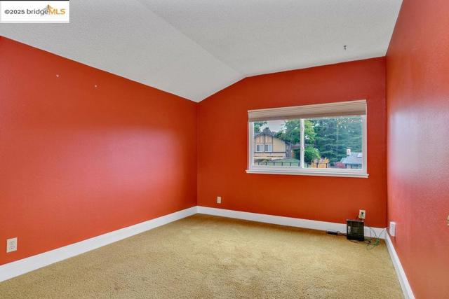 Carpeted spare room featuring vaulted ceiling and baseboards