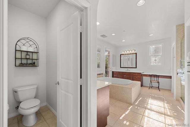 Primary suite toilet room and spa bathroom with double sinks, oversized bath tub, walk in shower, and two walk in closets. two doors leading out to covered outdoor patio overlooking the gorgeous back yard and pool with mountain views.