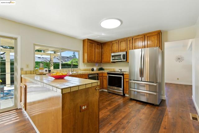 Kitchen with appliances with stainless steel finishes, brown cabinets, dark wood-type flooring, and tile countertops