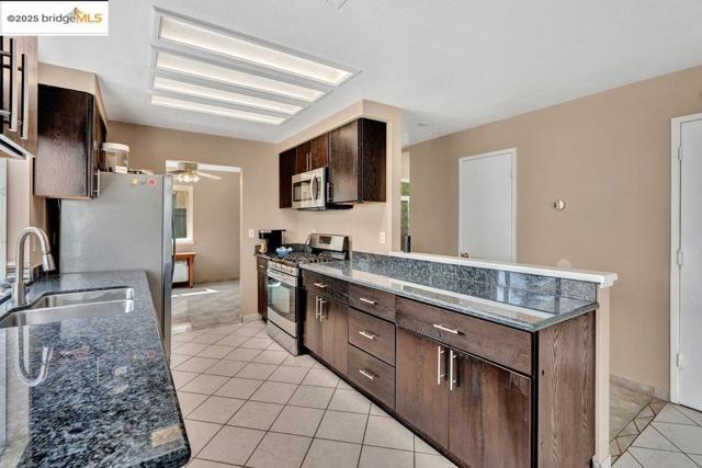 Kitchen with light tile patterned floors, stainless steel appliances, dark brown cabinetry, a ceiling fan, and a peninsula