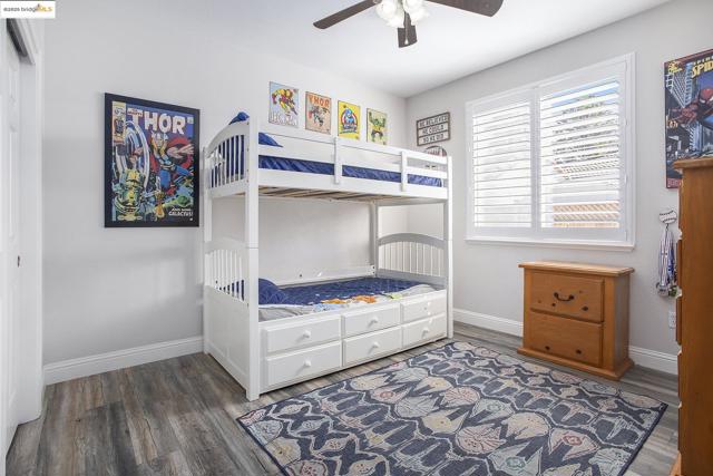 Bedroom with a ceiling fan, laminate wood-type flooring, and shutters for window covering.