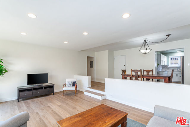 Open-plan living and dining area with light wood floors, a wood coffee table, and kitchen beyond.