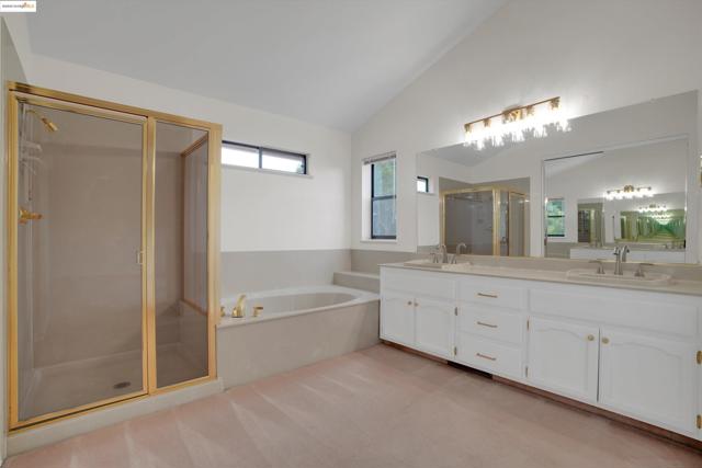Bathroom featuring a bath, a stall shower, double vanity, lofted ceiling, and light carpet