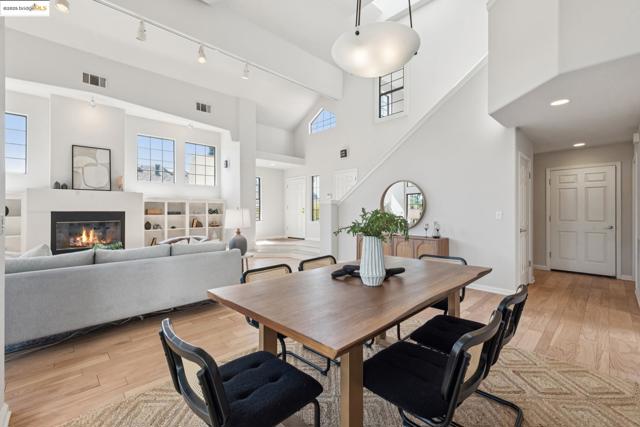 Dining area featuring light wood-type flooring, a glass covered fireplace, a high ceiling, track lighting, and beam ceiling